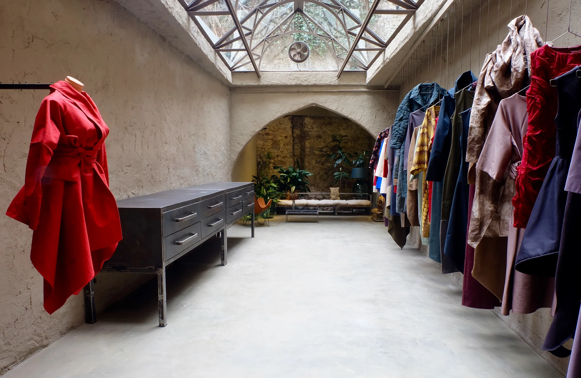 A red garment and hanging garments beneath the glass roof of the atelier